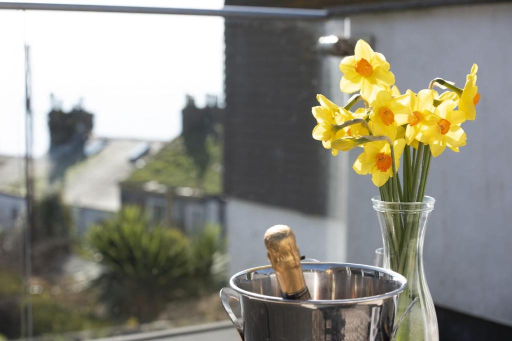 Eine Vase voller gelber Blumen neben einer Tasse. in der Unterkunft Mousehole View in Mousehole