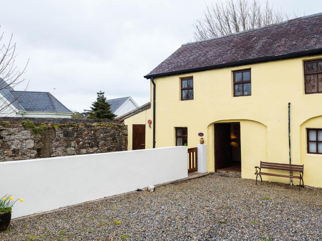 una casa amarilla con una pared blanca y un banco en The Stable en Fethard on Sea