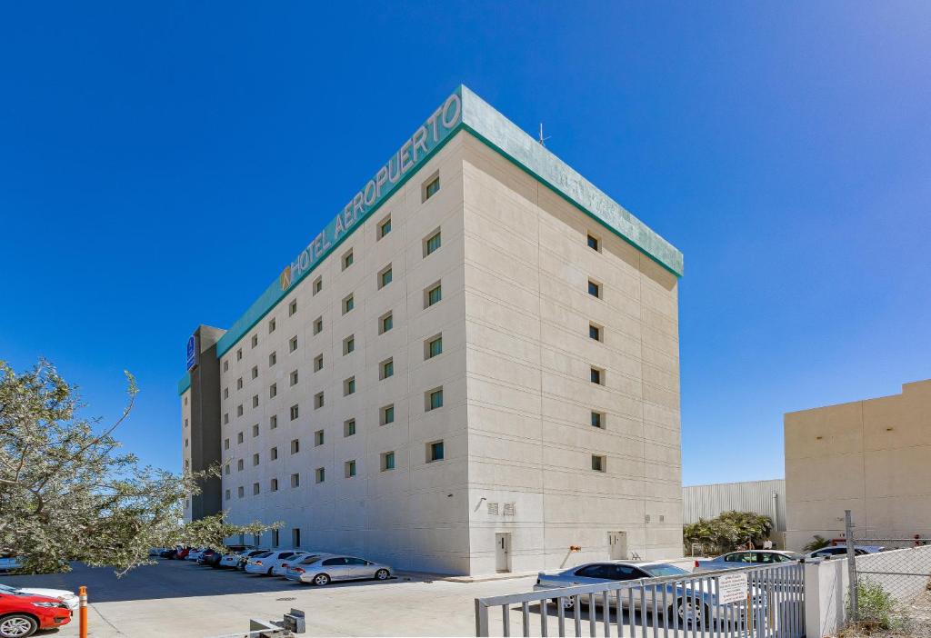 a hotel building with cars parked in a parking lot at Hotel Aeropuerto Los Cabos in San José del Cabo