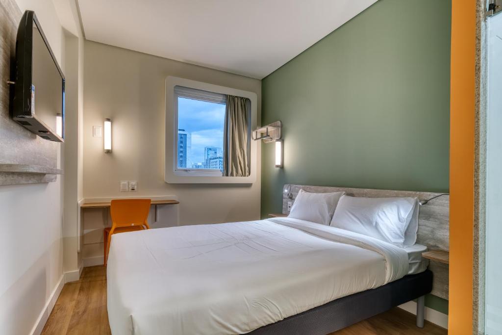 um quarto com uma cama, uma secretária e uma janela em ibis budget BH Savassi em Belo Horizonte