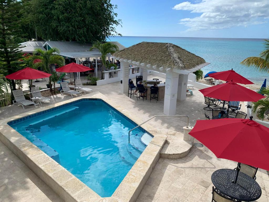 a swimming pool with red umbrellas and the ocean at Sand Castle on the Beach - Adults Only in Frederiksted