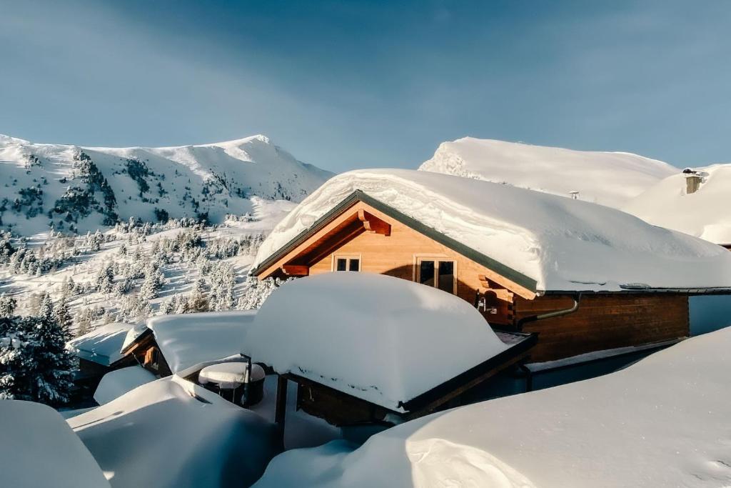 a cabin covered in snow with mountains in the background at Heidi Chalets Falkert Heidialm - Chalets Bergwinter in Patergassen