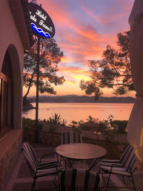 a patio with chairs and a table and a sunset at Hotel Cala Fornells in Paguera