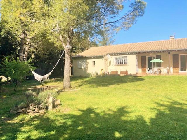 una hamaca en un patio junto a una casa en Villa 110m2, 7 pers, Jacuzzi , 3 chambres, terrain clos et arboré 2500m2 en Trèbes