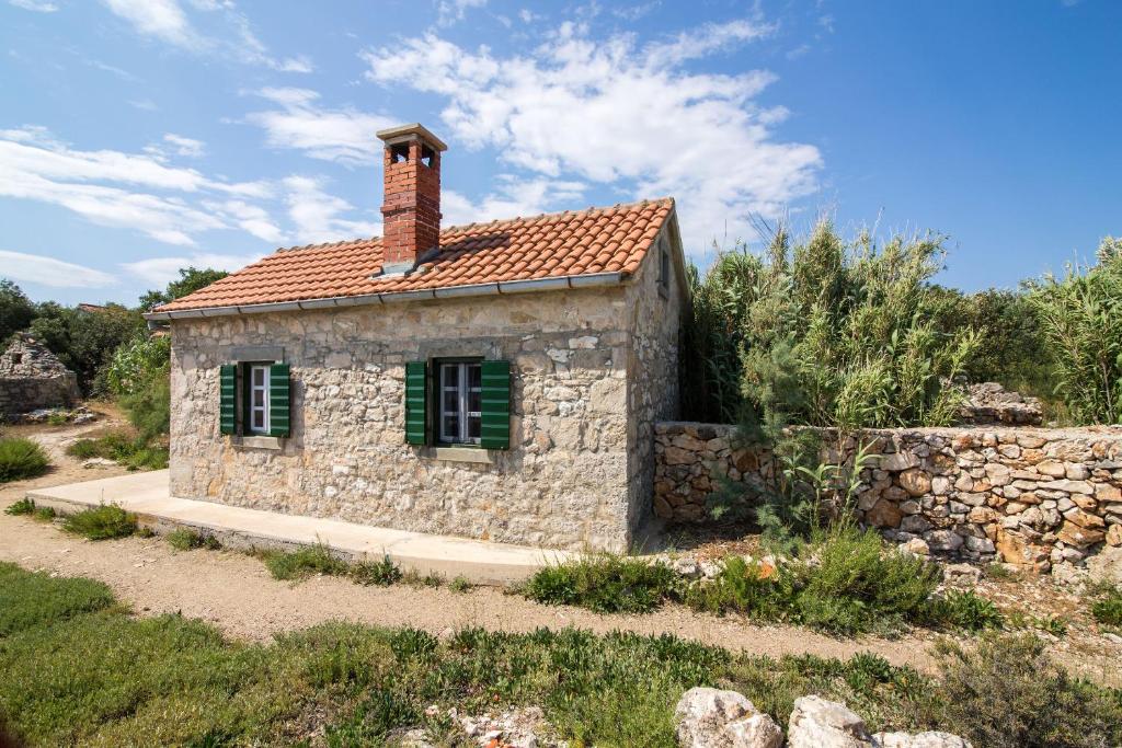 una casa in pietra con persiane verdi e un muro di mattoni di House Landjin a Pašman (Pasmano)