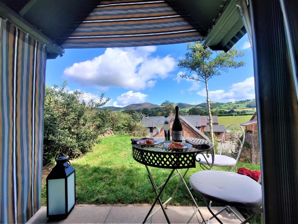 een patio met een tafel en stoelen en een fles wijn bij Curlew's Nest in Ruthin