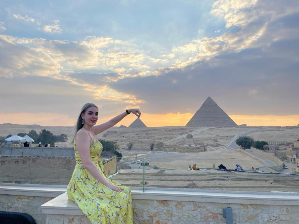 uma mulher de vestido amarelo sentada numa parede com as pirâmides em Giza Pyramids Inn no Cairo