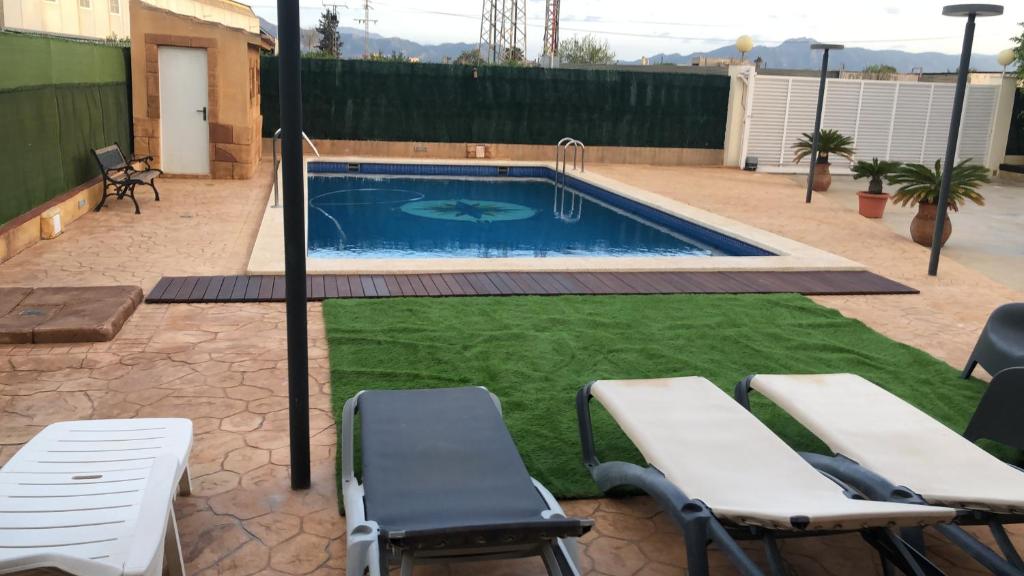 uma piscina com relva e cadeiras num quintal em Casa de invitados con piscina privada y WIFI em Múrcia