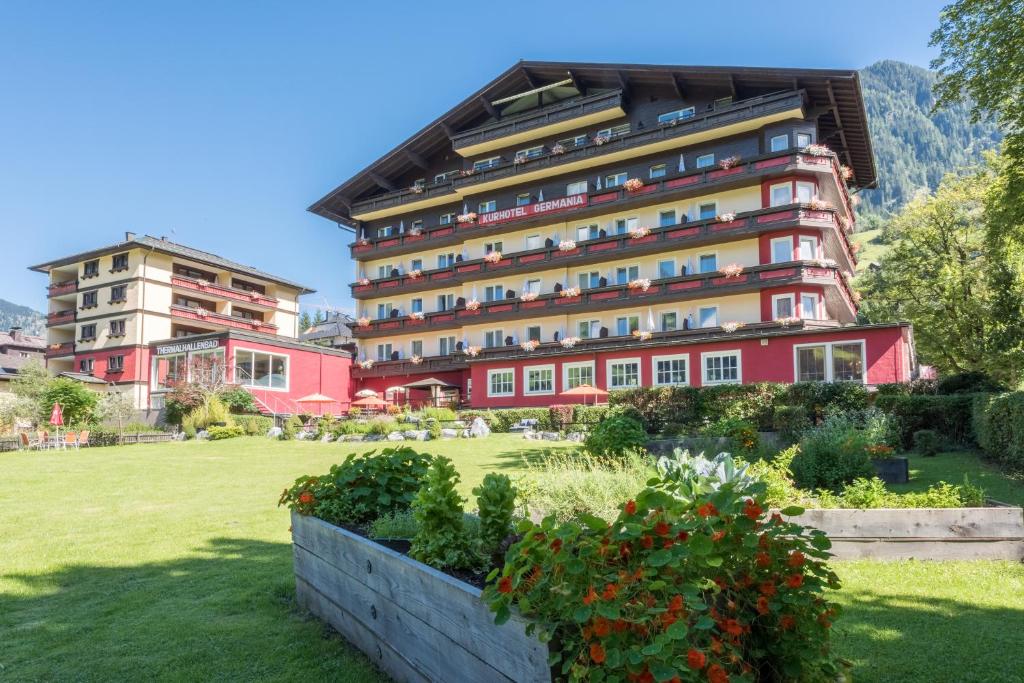 a large red building with a garden in front of it at Hotel Germania Gastein - ganzjährig inklusive Alpentherme Gastein in Bad Hofgastein