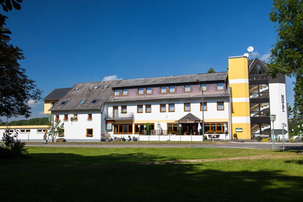 ein großes gelbes und weißes Gebäude mit einem Grasfeld in der Unterkunft Hotel Schoos in Fleringen