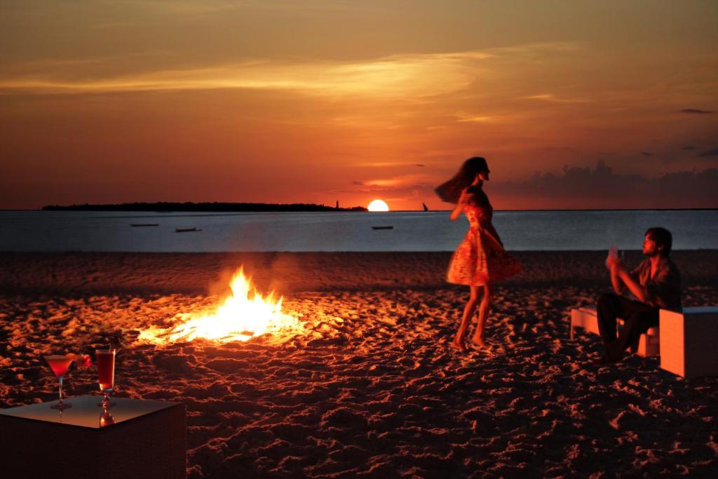 a woman standing on a beach with a bonfire at Gold Zanzibar Beach House & Spa in Kendwa