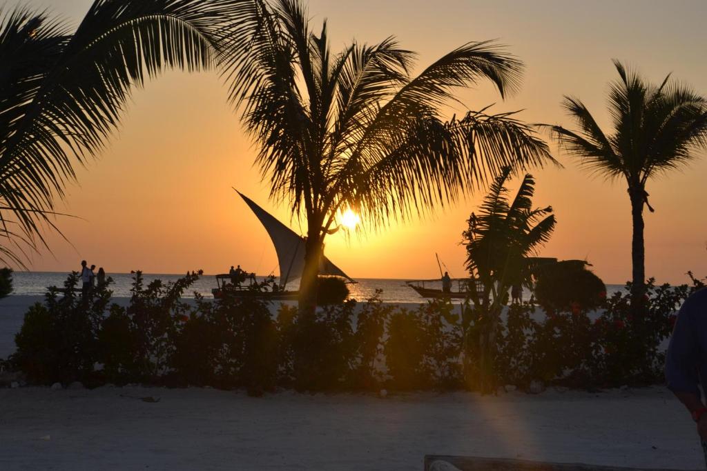 a sunset on the beach with a boat and palm trees at Gold Zanzibar Beach House & Spa in Kendwa