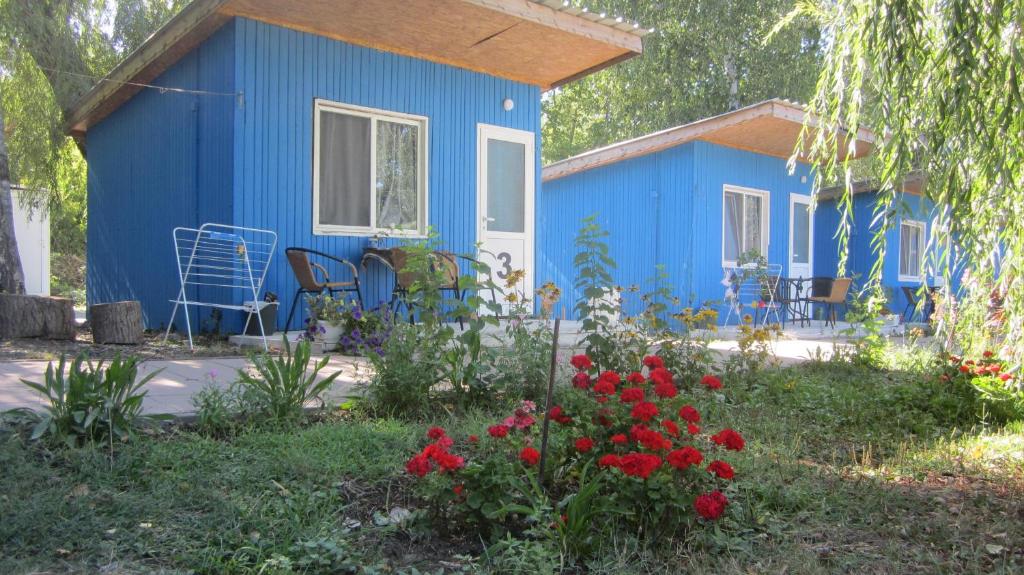 une petite maison bleue avec des fleurs rouges dans la cour dans l'établissement Къмпинг - Бунгала "НЕСТИНАРКА", Царево Camping - Bunglalows "NESTINARKA", Tzarevo, à Tsarévo