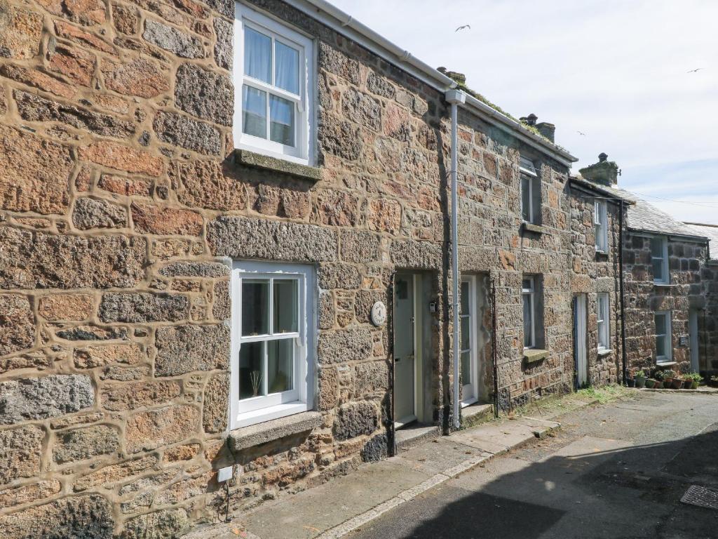 an old stone house with white windows on a street at Mural Cottage in Mousehole