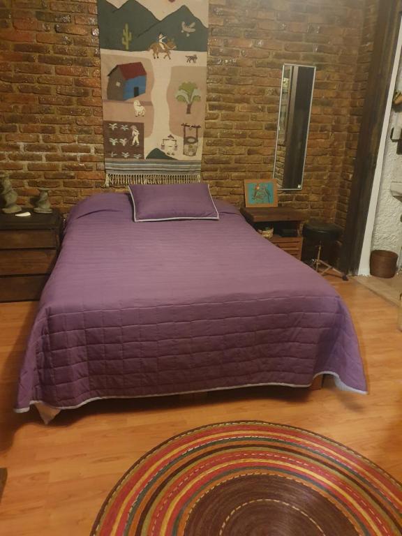 Cama morada en habitación con pared de ladrillo en Cerca del Colmex, Flacso y U Pedagogica, en Ciudad de México