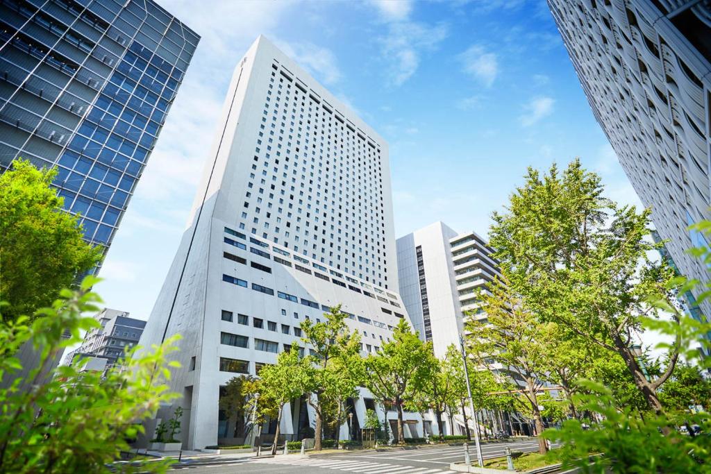 a tall white building in a city with trees at Hotel Nikko Osaka in Osaka