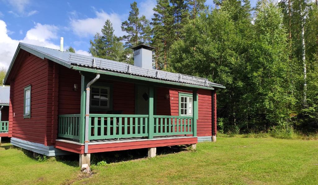 een rode hut met een groene veranda op een veld bij Ekesberget Stugby Stuga 8 in Ekshärad
