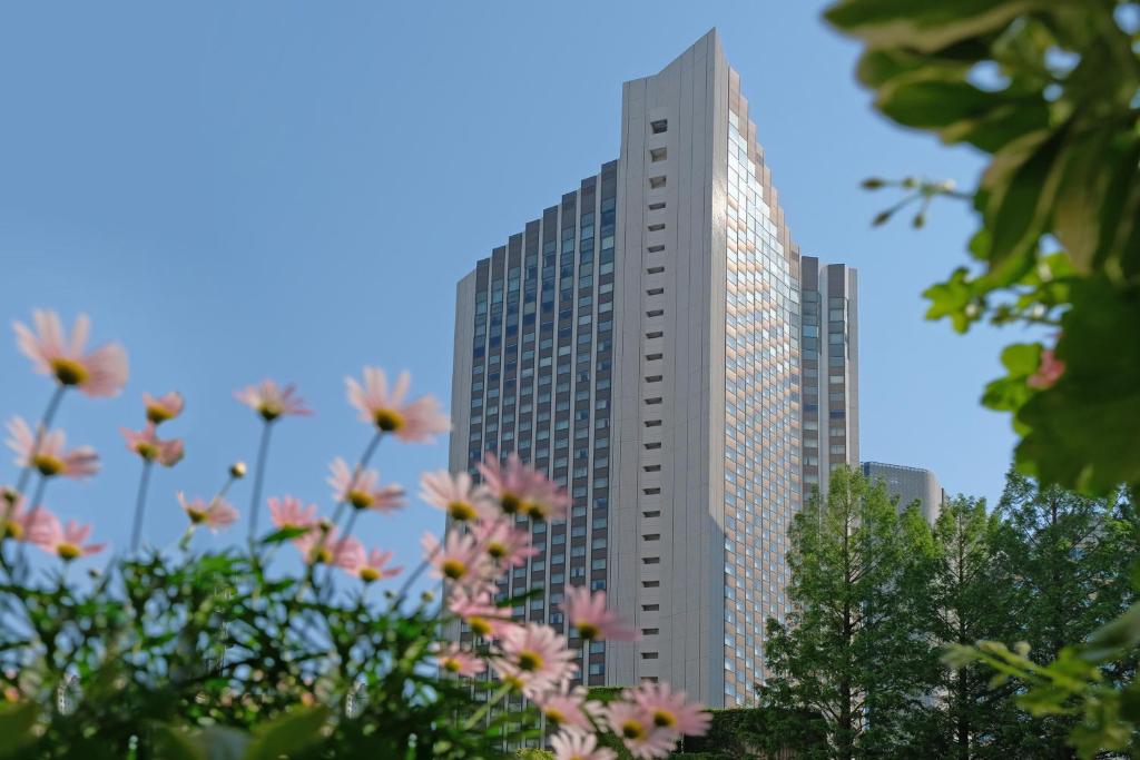 Um edifício alto com flores cor-de-rosa à frente. em ANA InterContinental Tokyo, an IHG Hotel em Tóquio