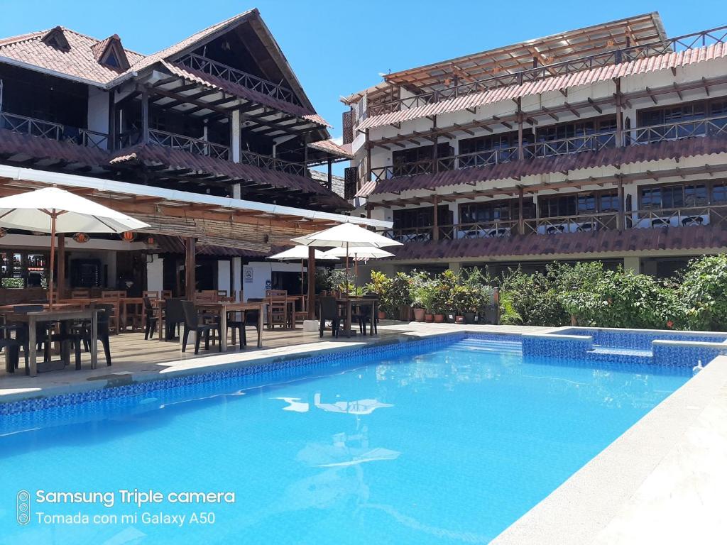 a swimming pool in front of a building with tables and umbrellas at Hotel La Vista in Canoa