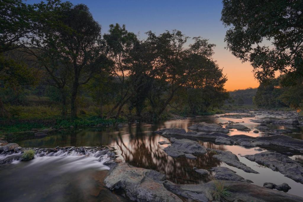 a river with rocks and trees at sunset at Agraharam Resorts in Thirunelli