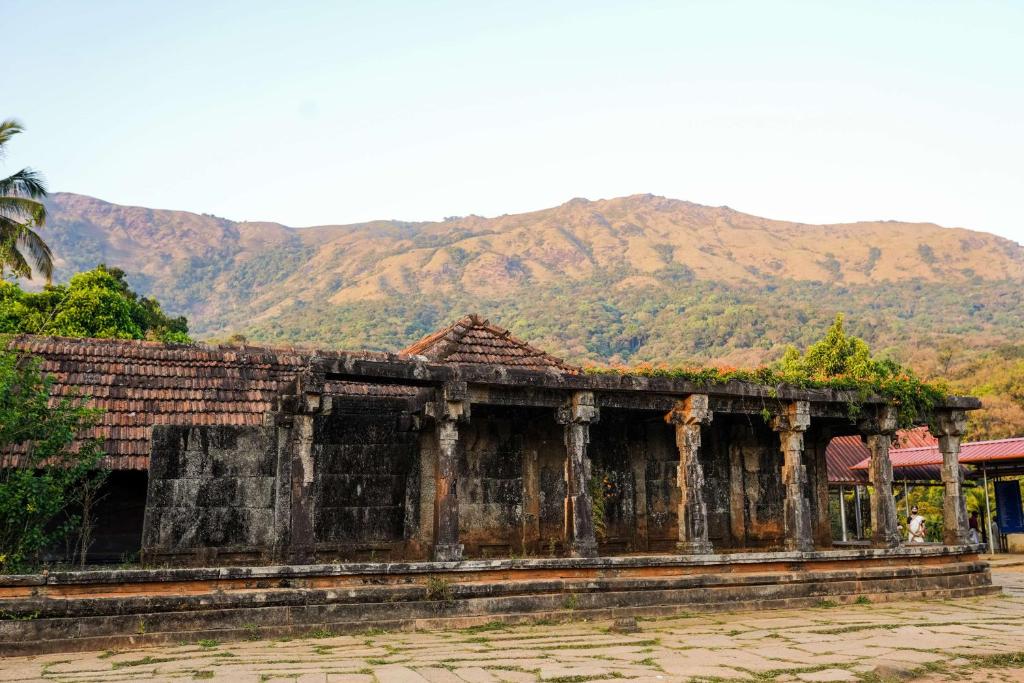 an old building with mountains in the background at Agraharam Resorts in Thirunelli