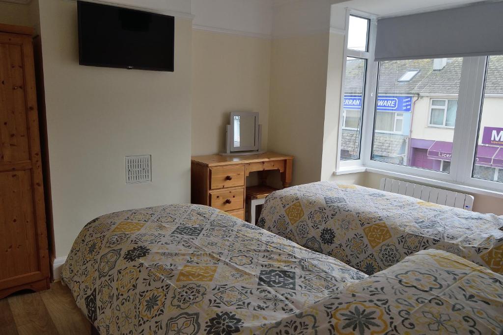 a bedroom with two beds and a tv on the wall at Darjeeling in Perranporth