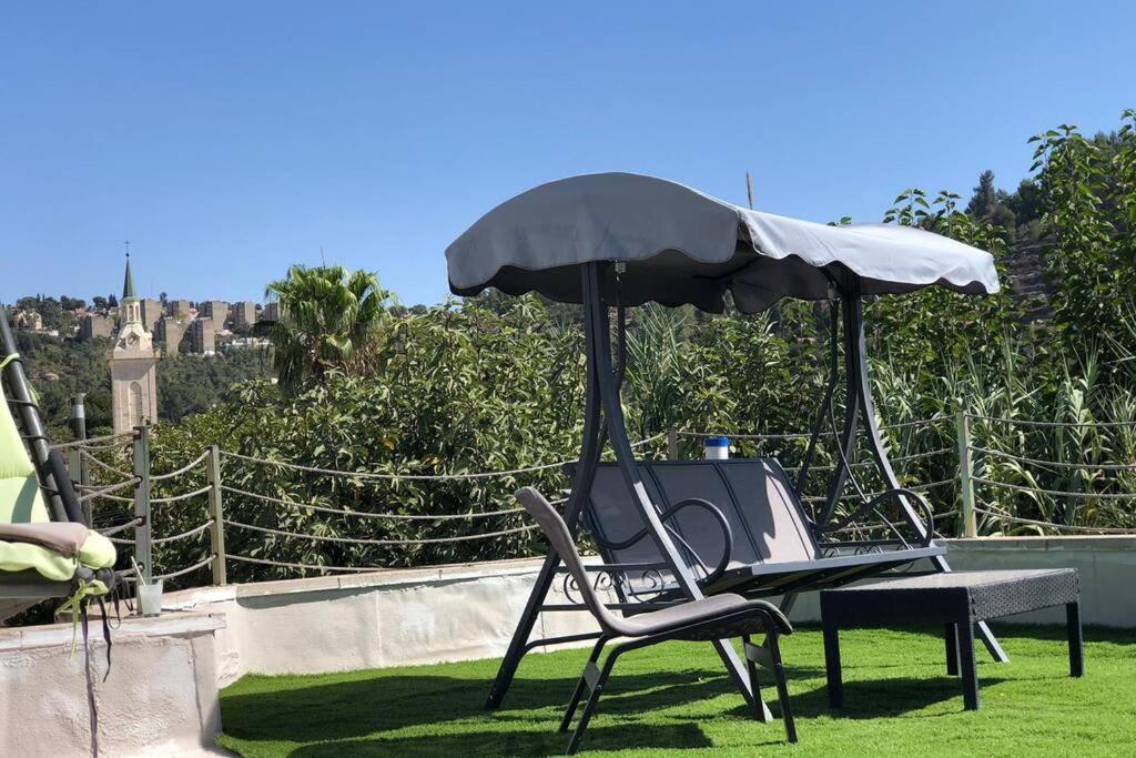 a chair sitting under an umbrella on the grass at דירת נופש - עין כרם in ‘En Kerem