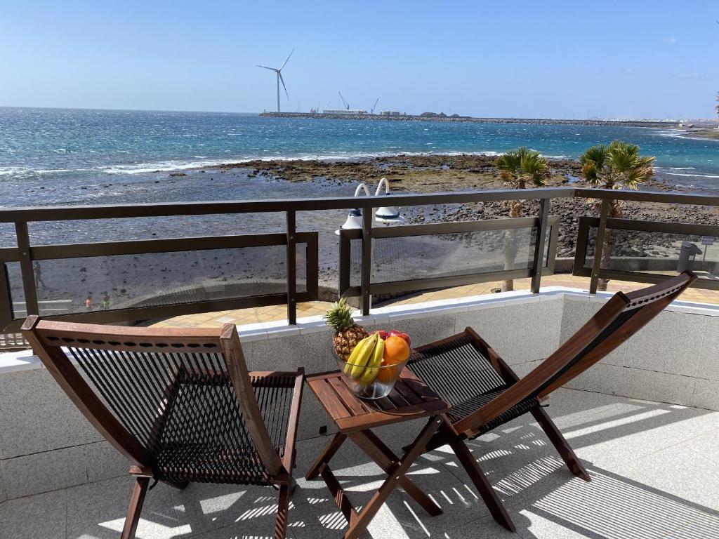 uma mesa com uma tigela de fruta e uma cadeira numa varanda com vista para a praia em Arinaga Colors em Arinaga