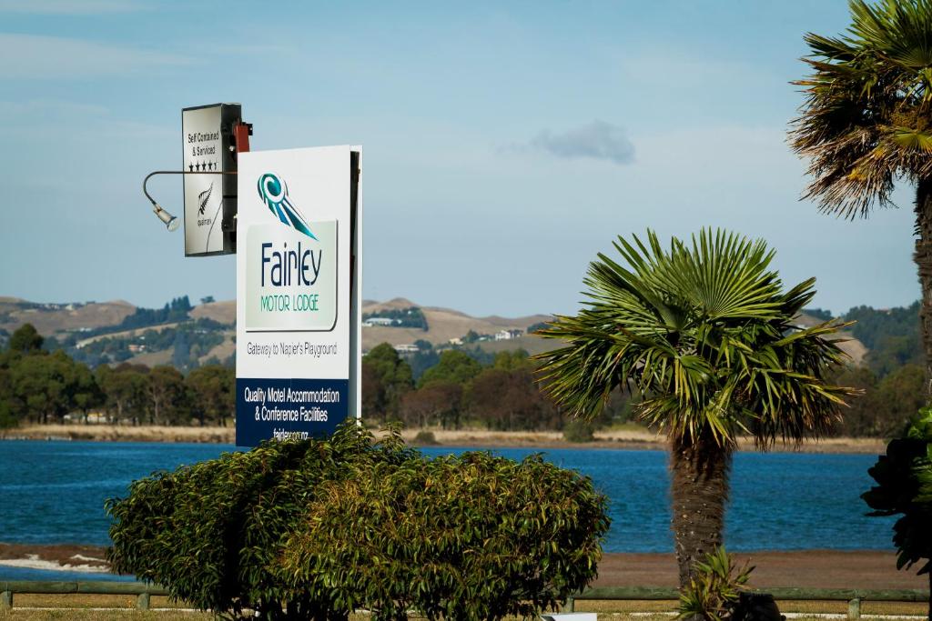 um sinal na frente de um corpo de água com uma palmeira em Fairley Motor Lodge em Napier