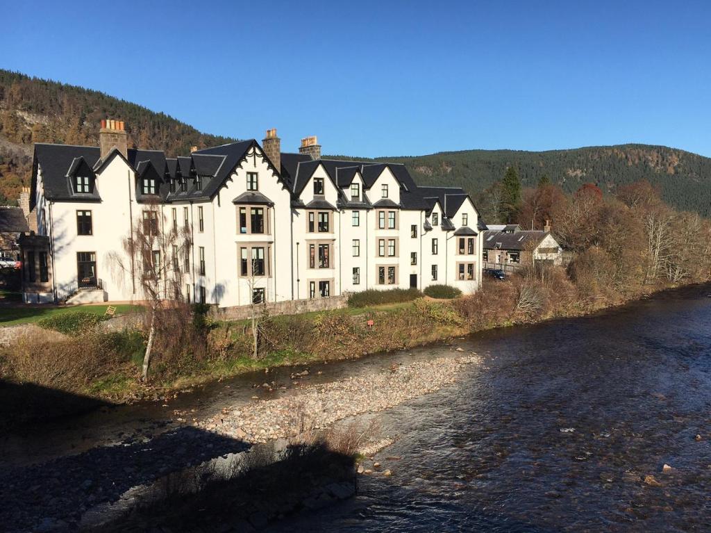 a large white house on the side of a river at Lovely 2 bedroom apt in Ballater on the River Dee in Ballater