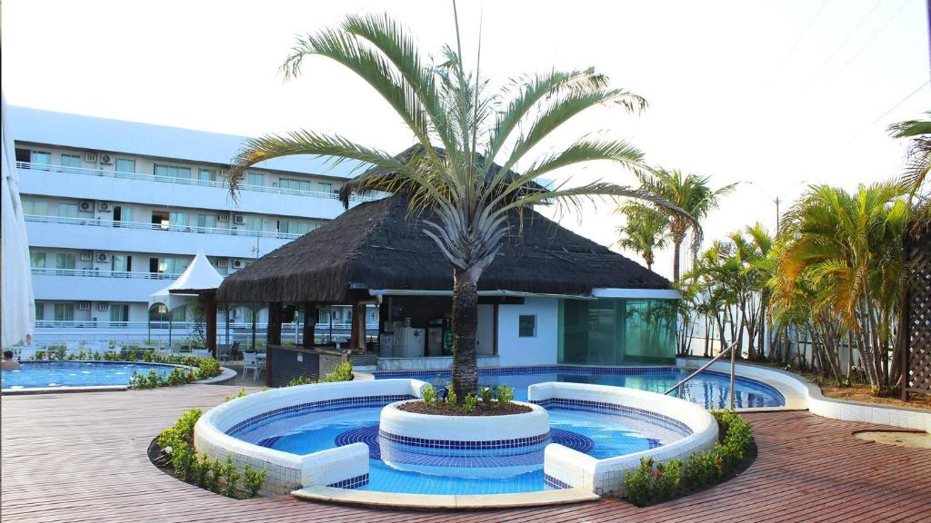 a pool with a palm tree in front of a hotel at Blue Marlim 2 quartos vista mar por Carpediem in Parnamirim