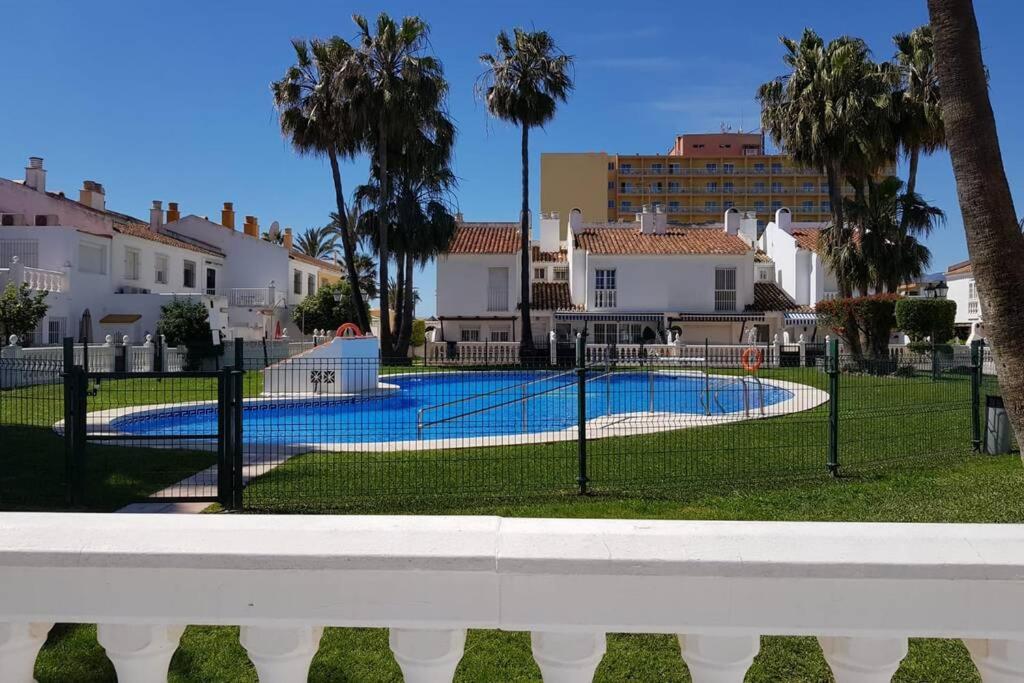 une clôture autour d'une piscine bordée de palmiers et de maisons dans l'établissement BEACH HOUSE Guadalmar, à Malaga