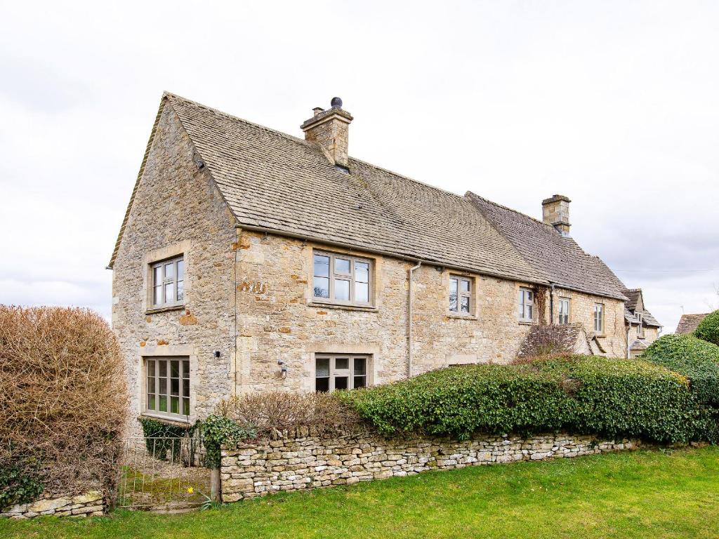 una antigua casa de piedra con un muro de piedra en Gardeners Cottage, en Chipping Norton