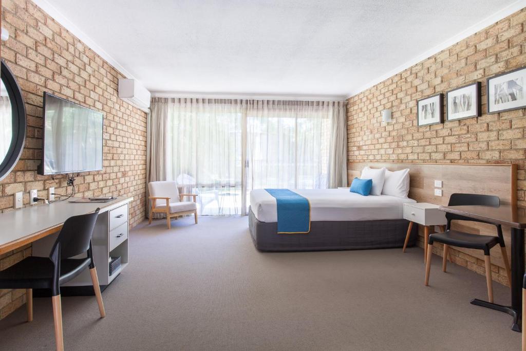 Sunshine Coast Motor Lodge في Woombye: غرفة فندقية بسرير وطاولة وكراسي