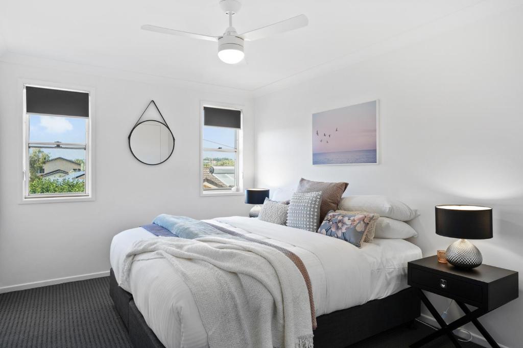 a white bedroom with a bed and two windows at Lennox Belle in Lennox Head