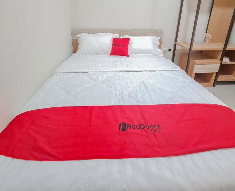 a red and white bed with a red pillow on it at RedDoorz Syariah @ Boemi Guesthouse Tasikmalaya in Tasikmalaya