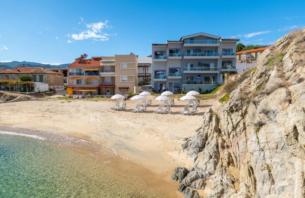 a beach with chairs and umbrellas in front of a building at Almare Seaside Studios & Suites - Sarti Sithonia in Sarti