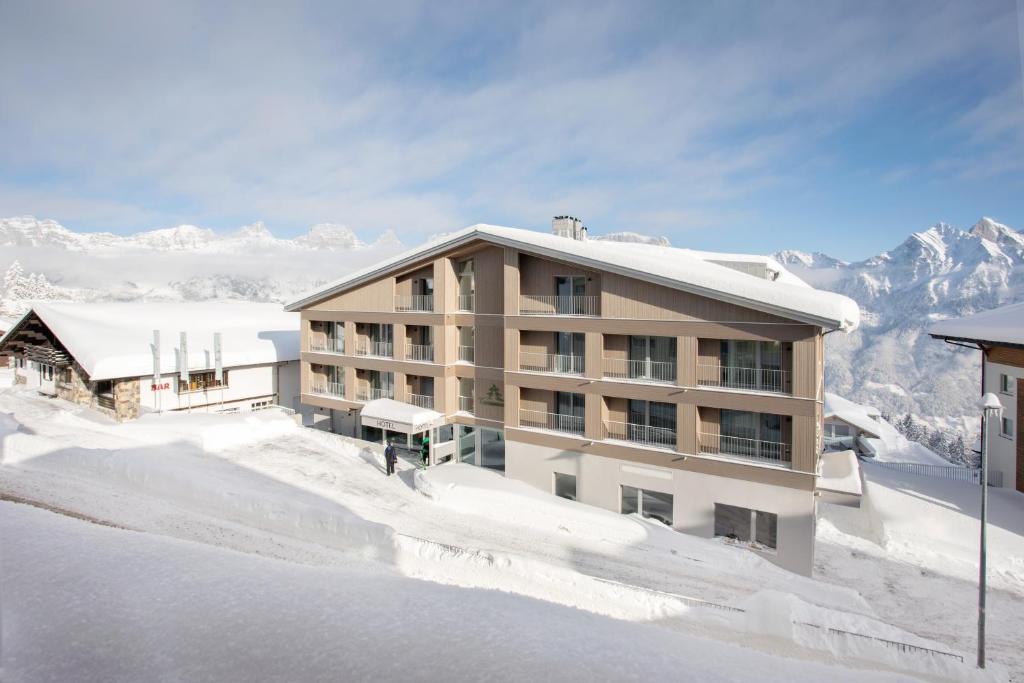 un edificio en la nieve con montañas en el fondo en Ferienwohnungen Tannenboden, en Flumserberg