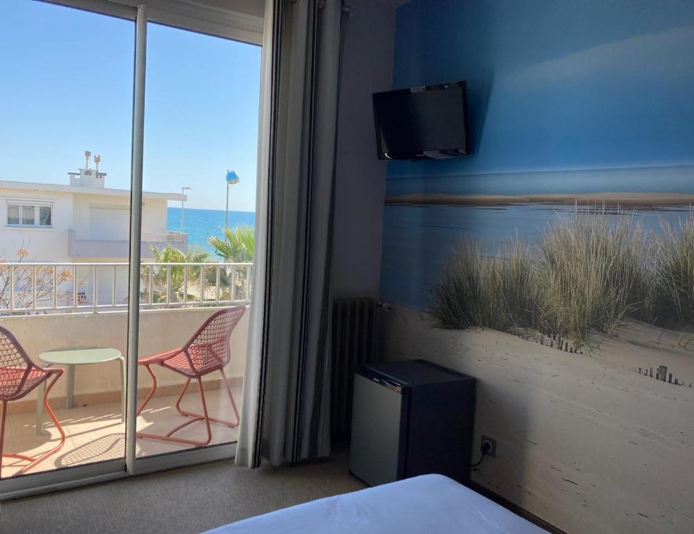 a bedroom with a view of a balcony with two chairs at Hôtel du Midi Plage in Palavas-les-Flots