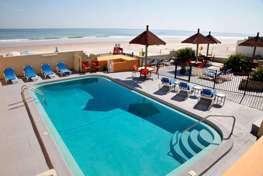 a swimming pool with chairs and a beach at Daytona Dream Inn By AmeriVu in Daytona Beach