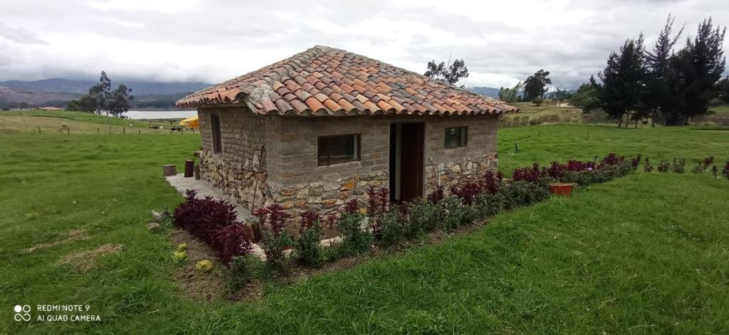 une petite maison en pierre dans un champ fleuri dans l'établissement Mirador Valle del Tomine - Cabaña vista al embalse, à Guatavita