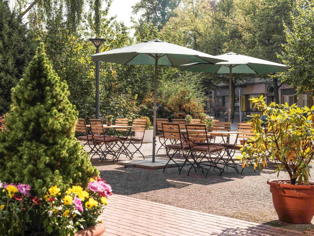 eine Terrasse mit Tischen, Stühlen, Sonnenschirmen und Blumen in der Unterkunft ibis Berlin City Nord in Berlin