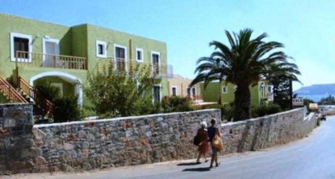 two people walking down a street next to a stone wall at Perla Apartments in Agia Pelagia