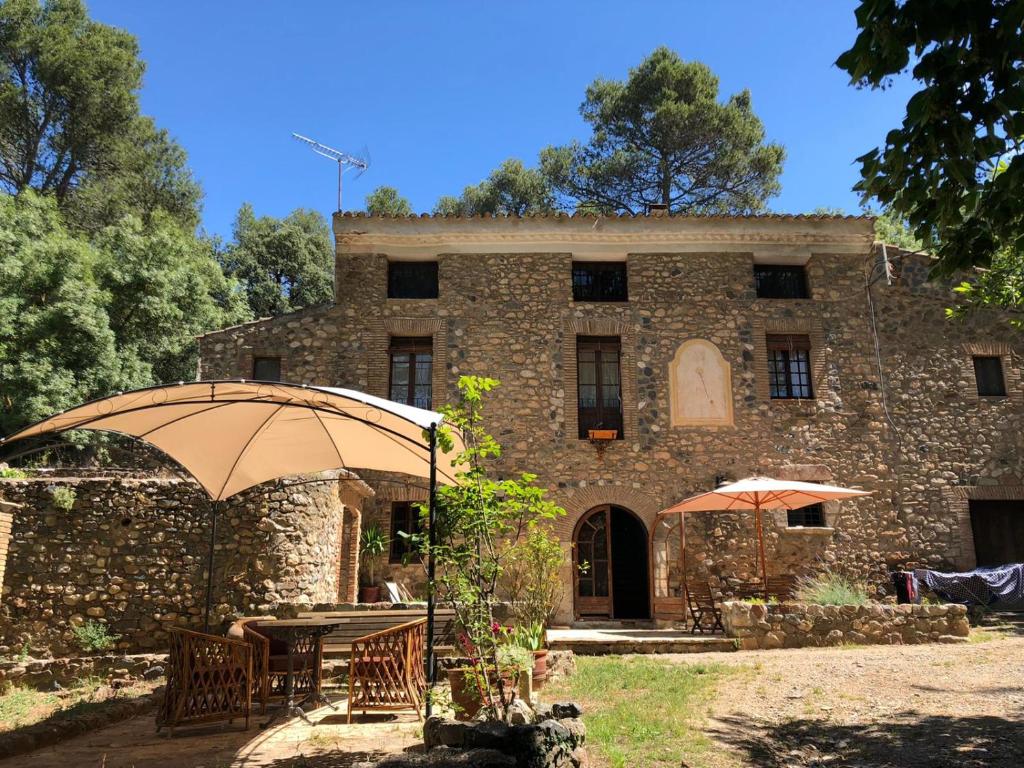 ein altes Steingebäude mit Tischen und einem Regenschirm in der Unterkunft Molí dels Aubins in Cornudella de Montsant
