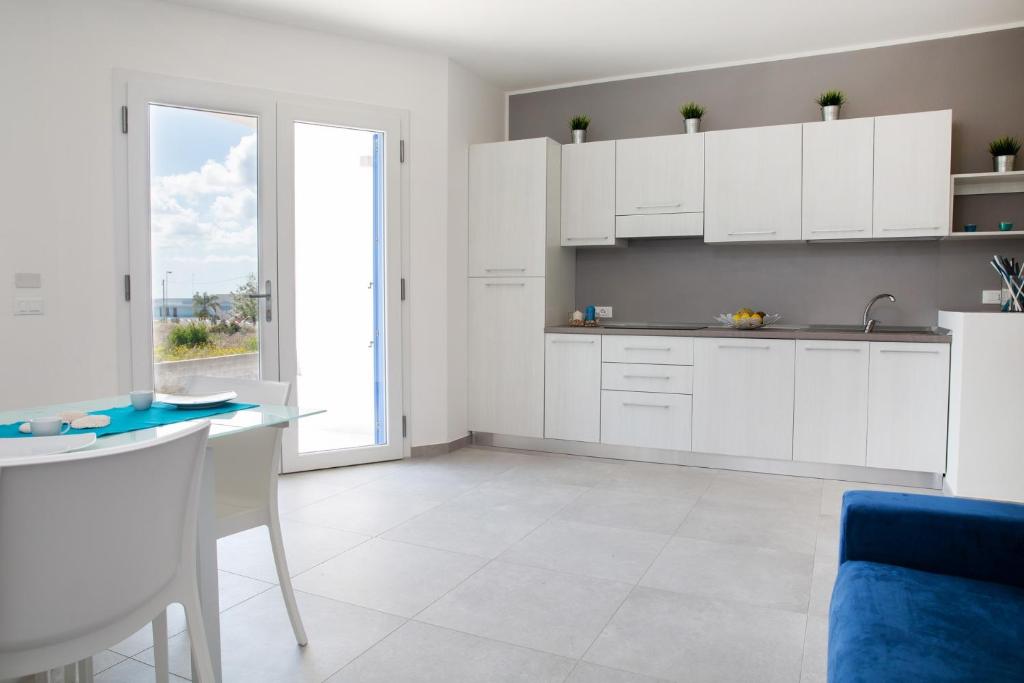 una cucina con armadi bianchi, tavolo e finestra di Residenziale Blu 1 a Marina di Pescoluse