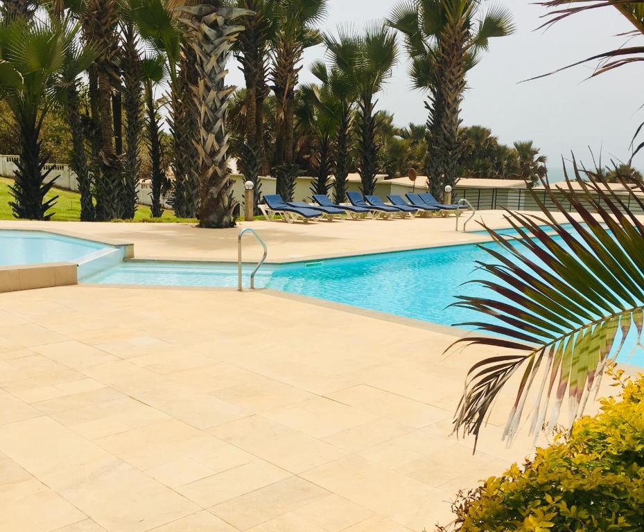 a swimming pool with palm trees and blue lounge chairs at Gambia Seafront Central in Bathurst