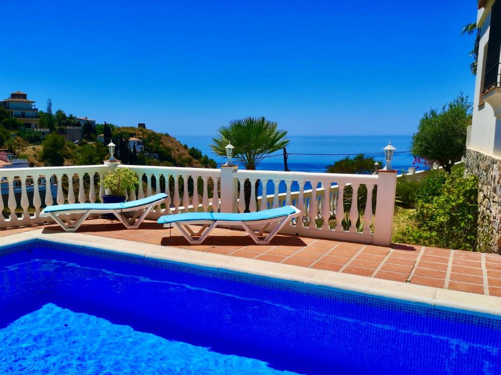a swimming pool with two chairs next to a white fence at House in a cove Almunecar in Almuñécar
