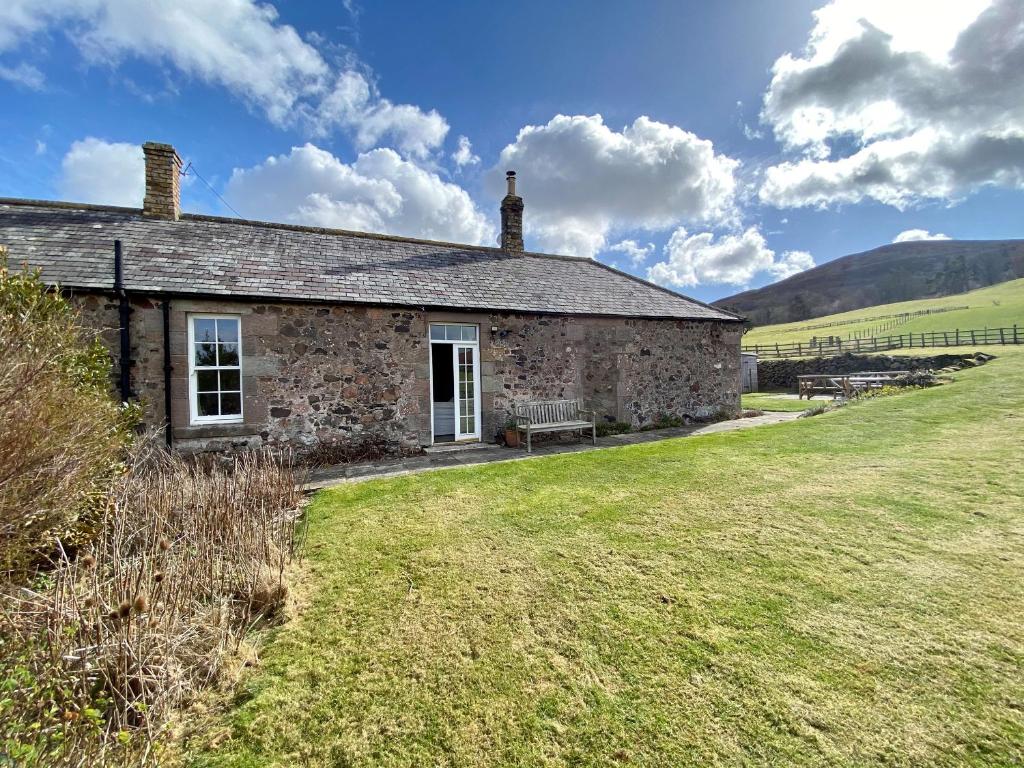 an old stone house with a bench in a field at Akeld Cottage in Akeld