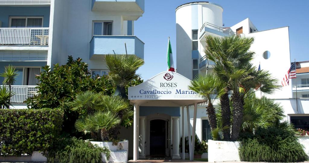 a building with a sign in front of palm trees at Hotel Cavalluccio Marino in Santa Marinella