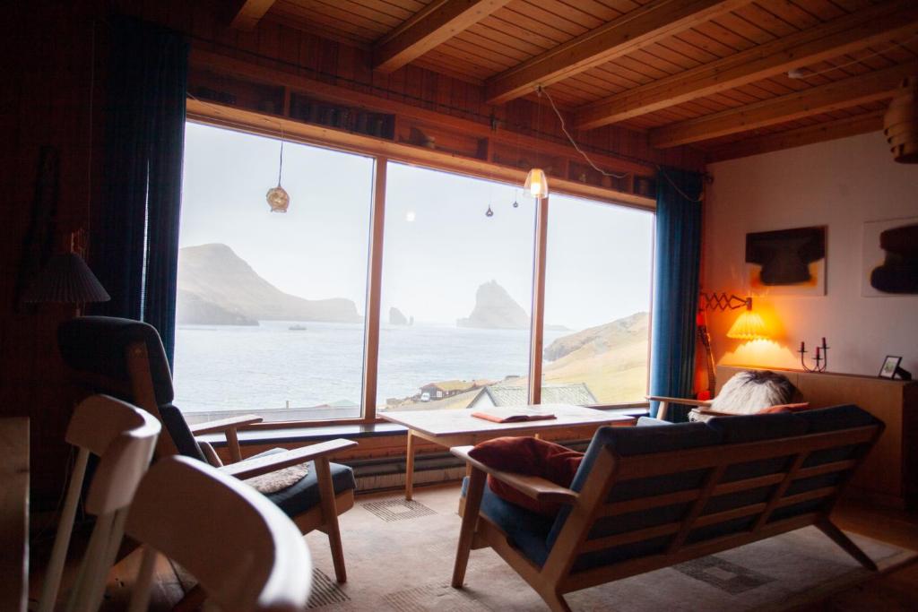 una persona sentada en una mesa en una habitación con una gran ventana en Idyllic Vacation Home with a Breathtaking View, en Bøur